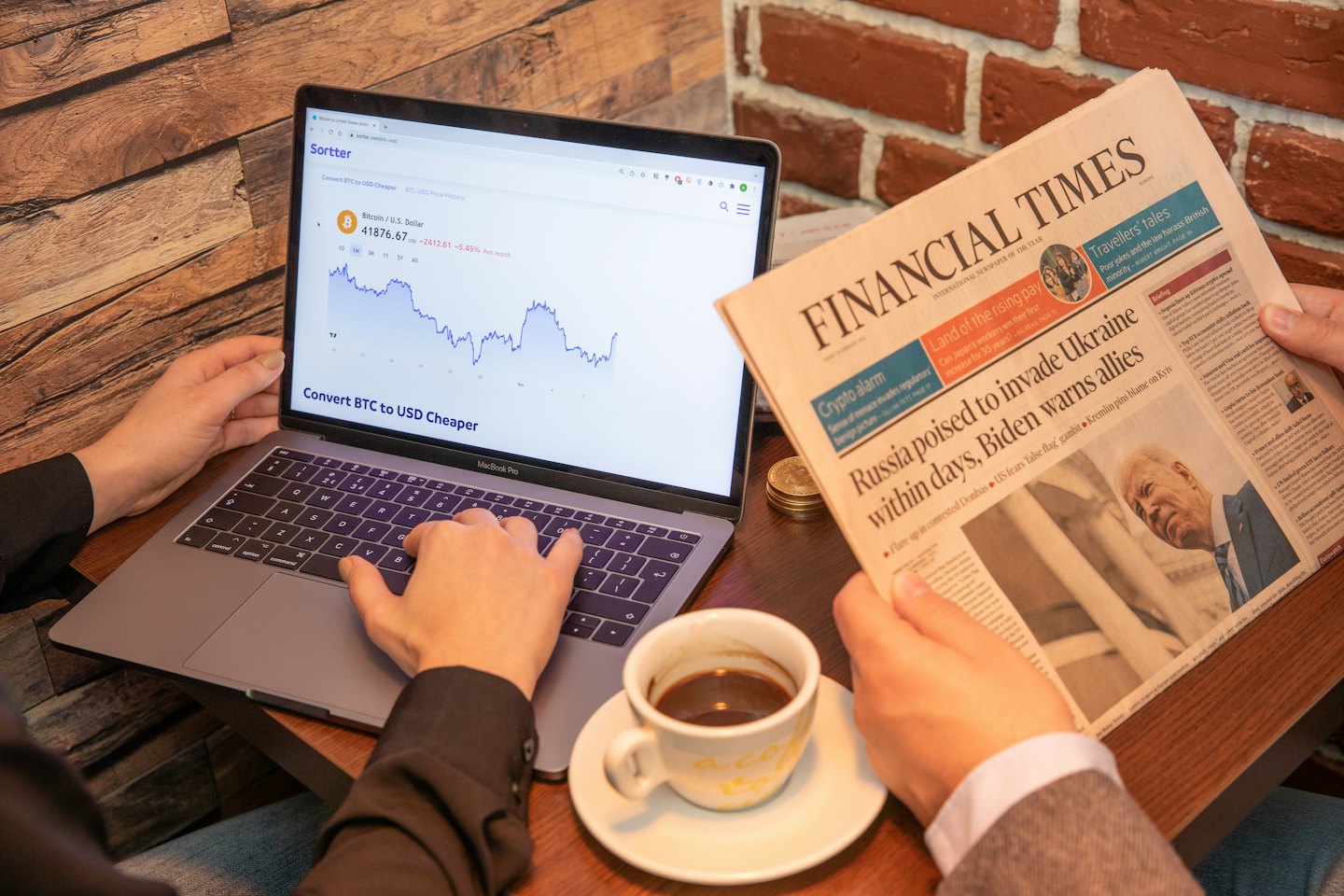 Bitcoin grafiği ve Financial Times gazetesinin gösterildiği dizüstü bilgisayarla etkileşimde bulunan eller.